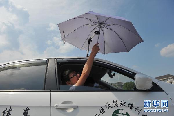 7月20日，在浙江省臨安市一家駕校內(nèi)，一名學(xué)員在車頂架著遮陽傘的教練車內(nèi)練習(xí)。