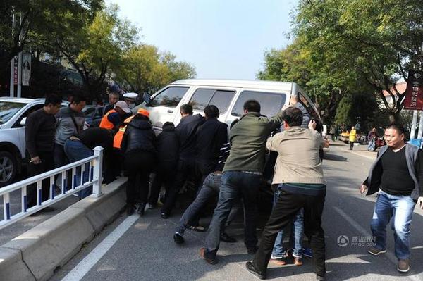 此時周圍路過的市民和附近商販紛紛趕來，十幾人用力抬起面包車，將老人救出。