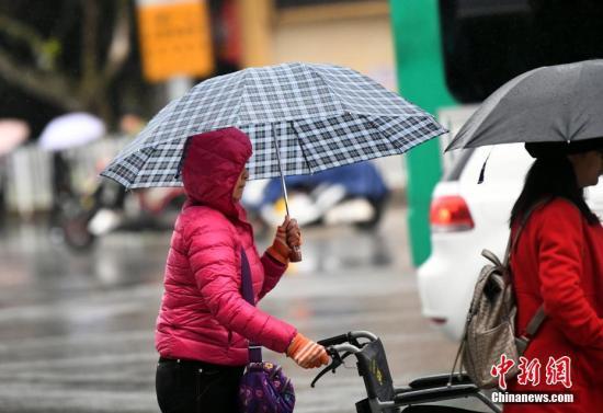 資料圖：昆明市區(qū)里身著羽絨服冒雨趕路的民眾。 中新社記者 李進紅 攝